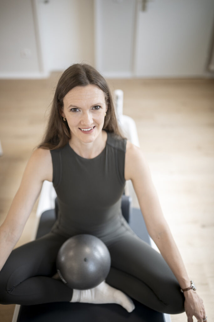 Trainerin mit Pilatesball auf dem Reformer bei MALEA Reformer Pilates Bad Krozingen
